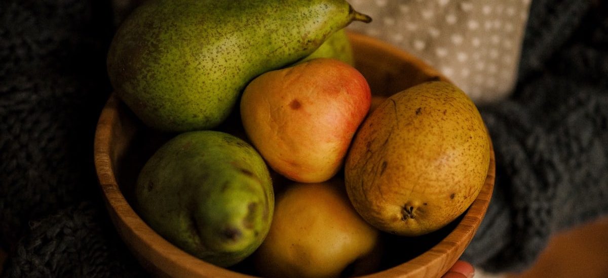 A wooden bowl filled with fresh pears, held outdoors on a sunny day.