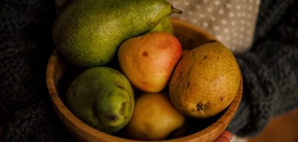 A wooden bowl filled with fresh pears, held outdoors on a sunny day.