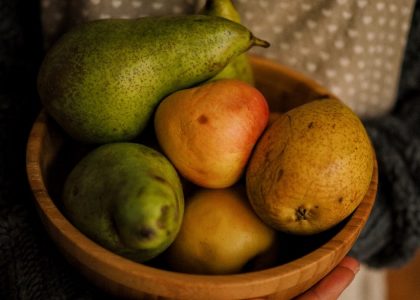 A wooden bowl filled with fresh pears, held outdoors on a sunny day.